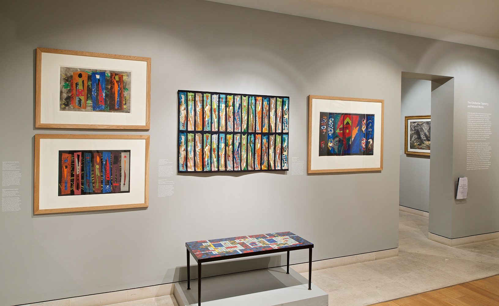 View of gallery showing four abstract wprks of art on the wall with a mosaic table below